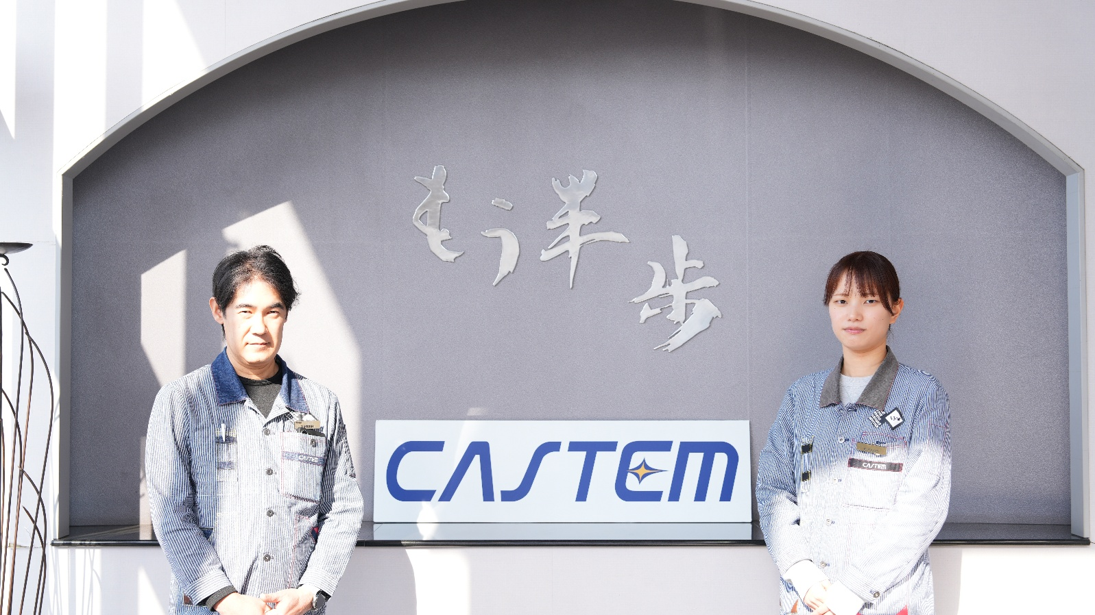 株式会社キャステムのご利用者様2名（同社入口のCASTEMロゴ前）